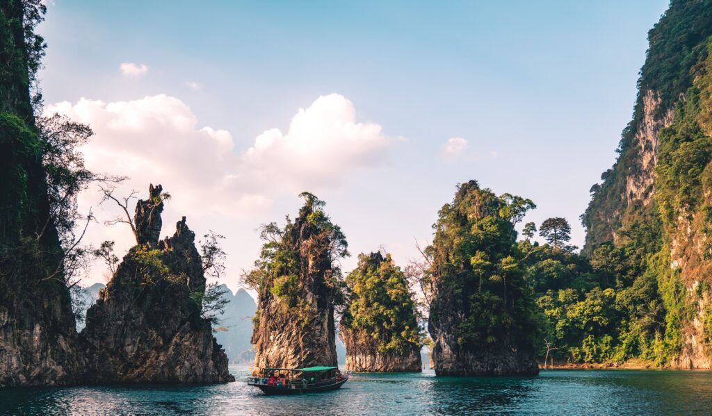 A traditional long-tail boat sailing past towering limestone karsts covered in greenery in Khao Sok National Park.
