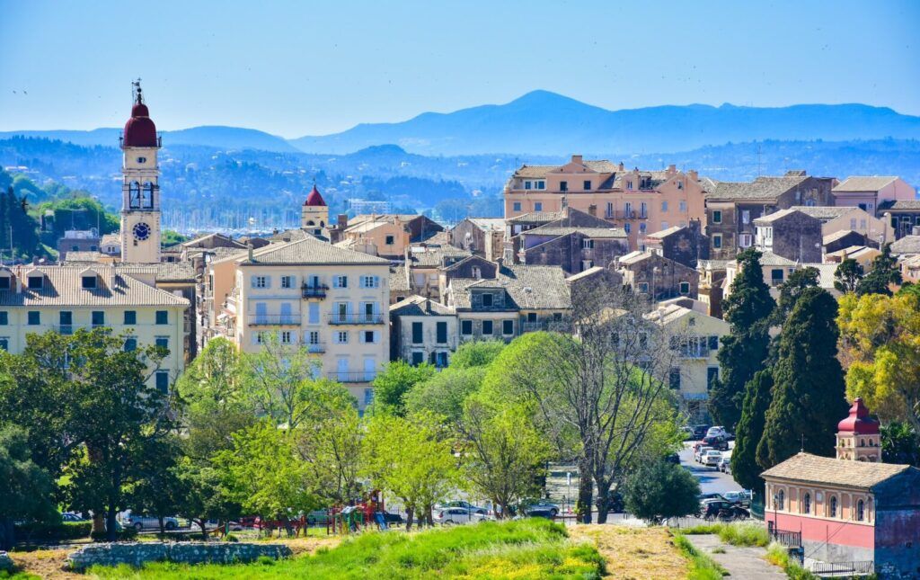White and brown buildings surrounded by trees and mountains in Corfu Town