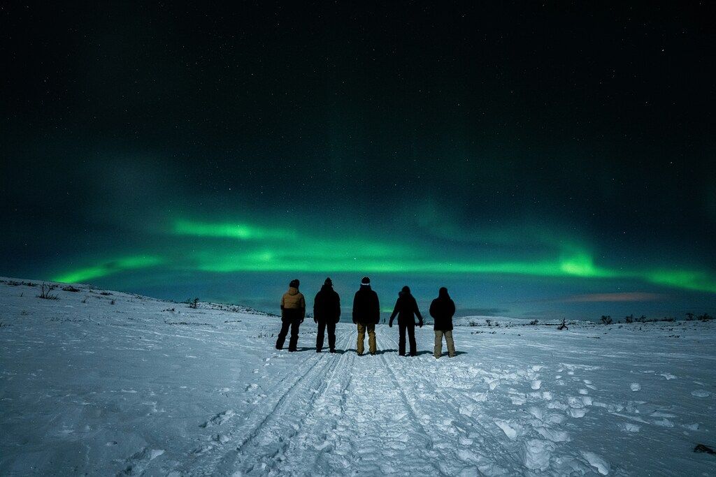 A group of people standing on the top of a snowy slope under the Northern Lights