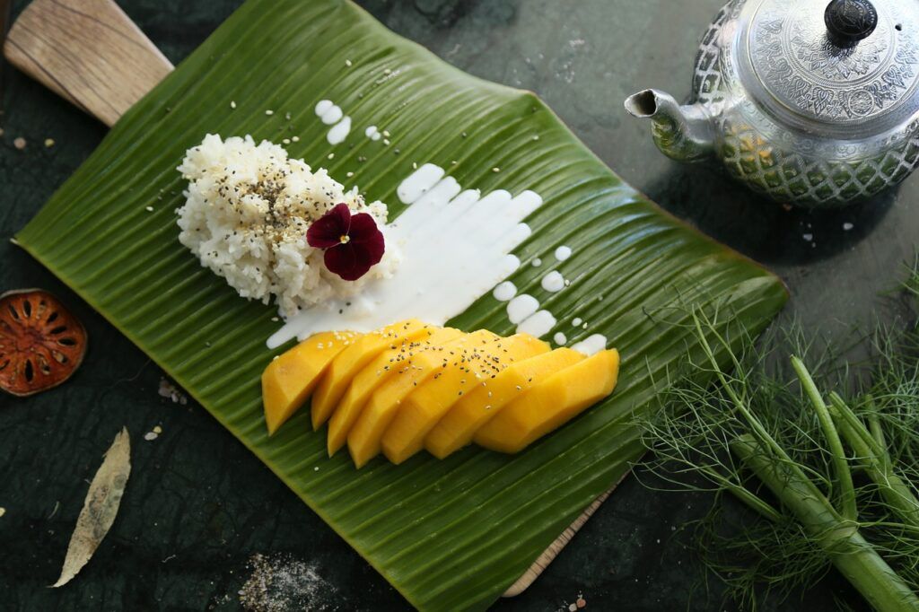 mango sticky rice on a green leaf and a teapot