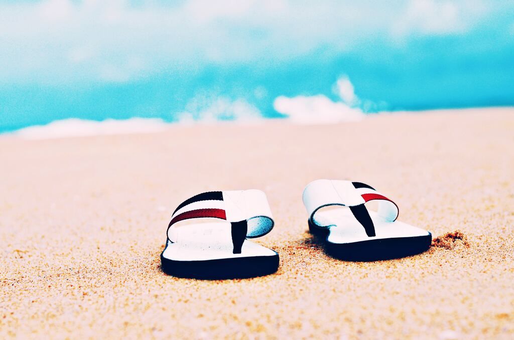 a pair of white flip-flops on the beach, with the sea behind