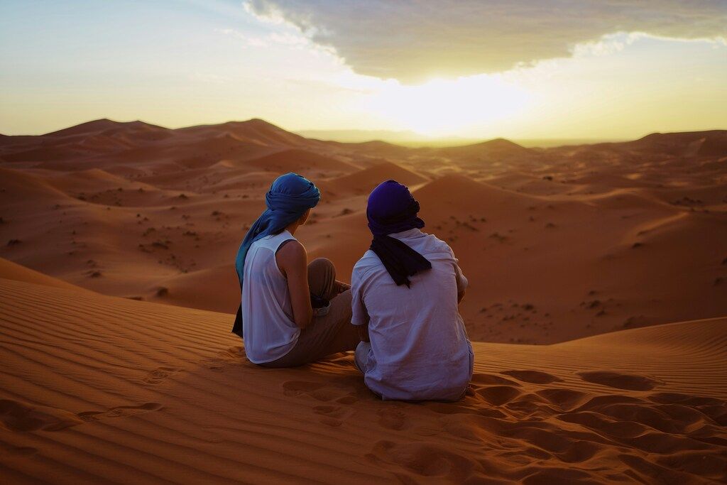 Two men sitting on sand dunes.