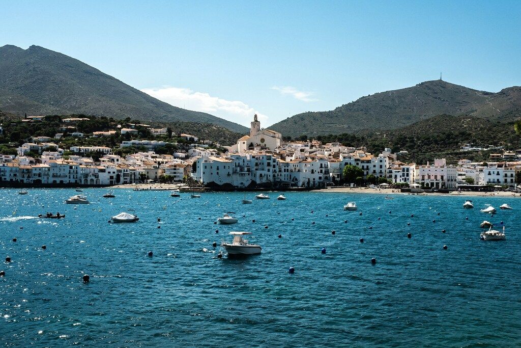 Seaside view of Cadaqués, a charming village with white buildings and boats in the water.