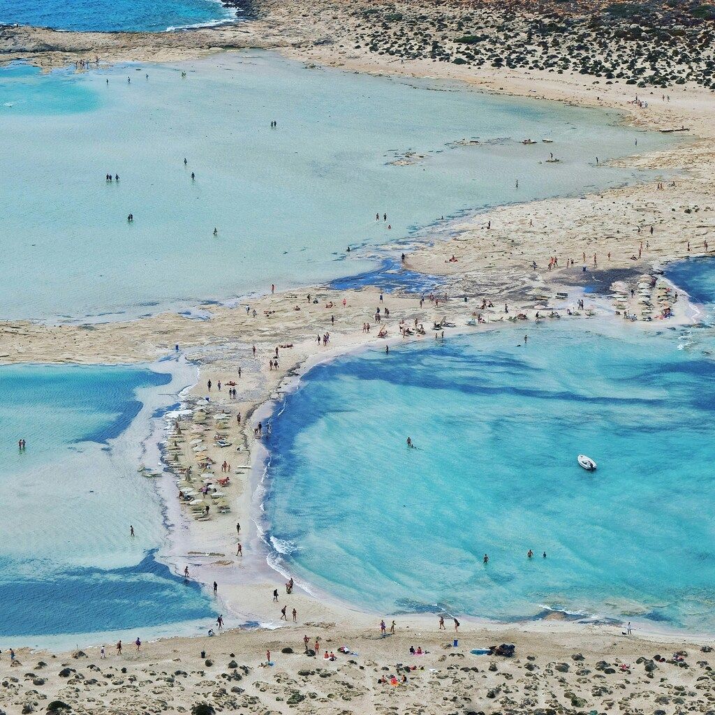 An aerial view of the stunning shallow waters and sandbars at Elafonissi Beach in Crete, with people relaxing and exploring the unique landscape