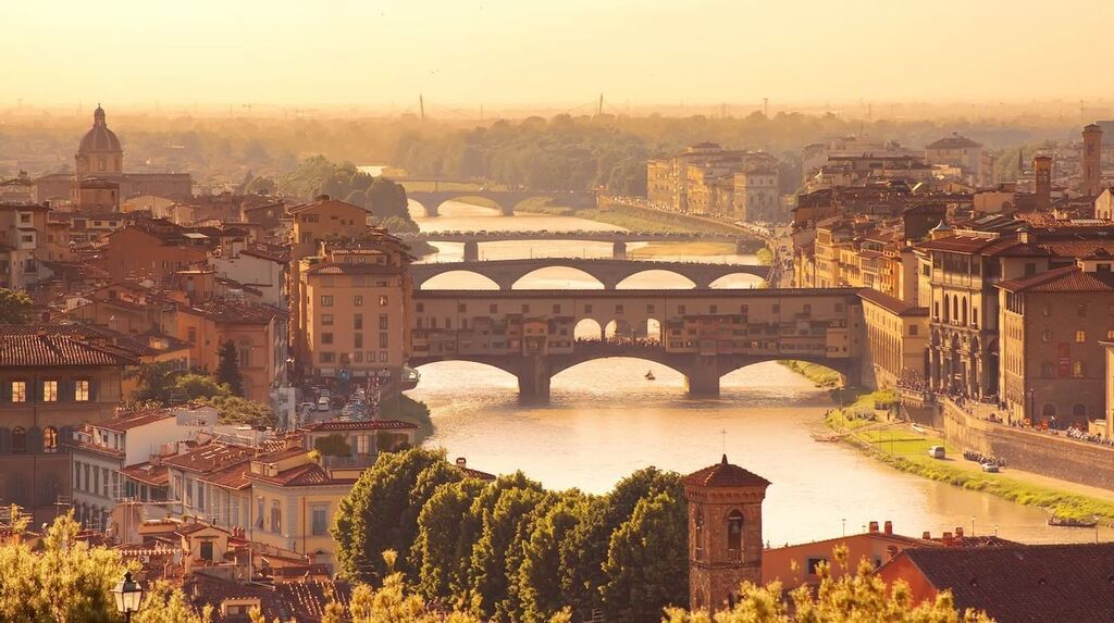 Aerial view of Florence, Italy, at sunset, with the Ponte Vecchio and other historic bridges spanning the Arno River