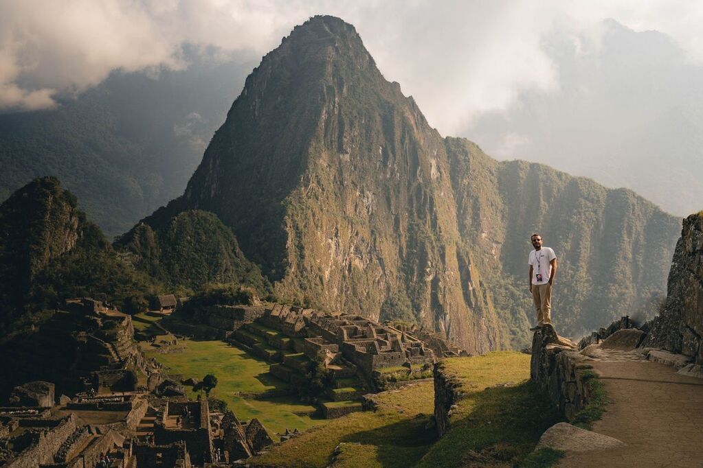 A man standing on a ledge at Machu Picchu, Peru, with the iconic Huayna Picchu mountain in the background