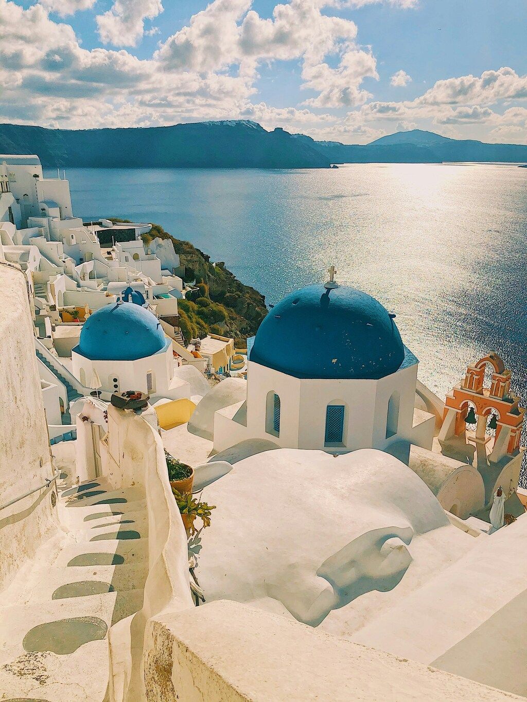 The iconic whitewashed buildings with blue domes of Santorini, set against the backdrop of the sparkling Aegean Sea under a sunny sky