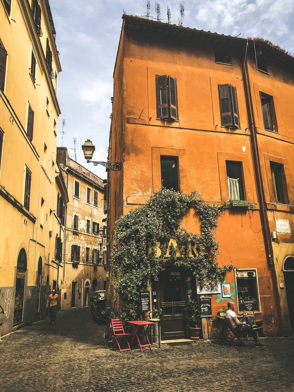 Charming street of in Rome with an orange building adorned by greenery and a small bar