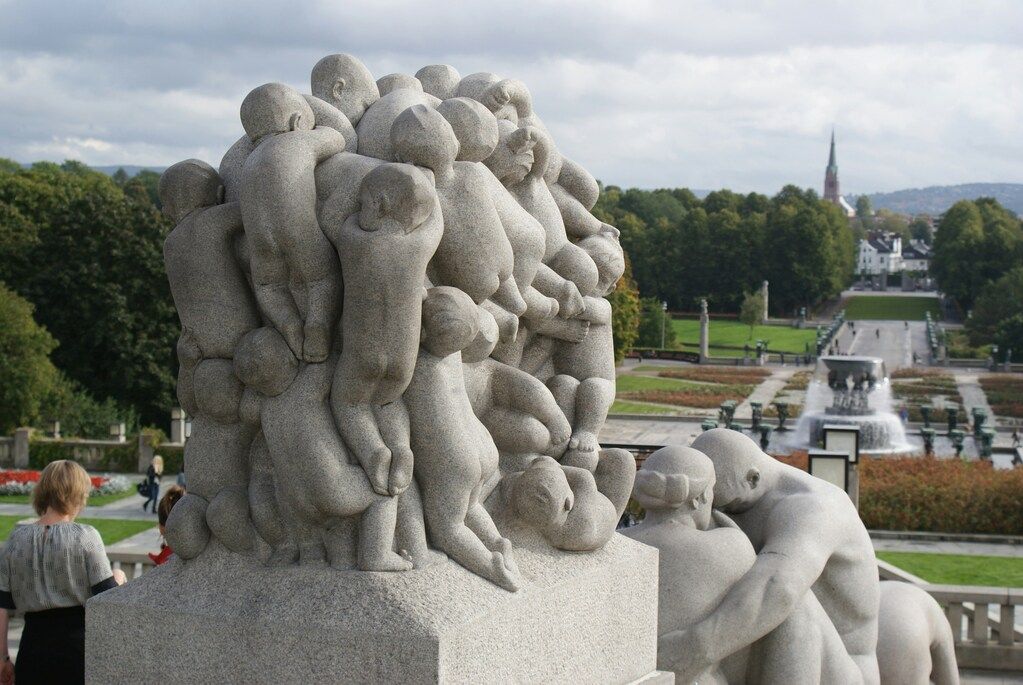 A sculpture at Vigelandsparken in Oslo, Norway, featuring intertwined human figures, with the park and cityscape in the background