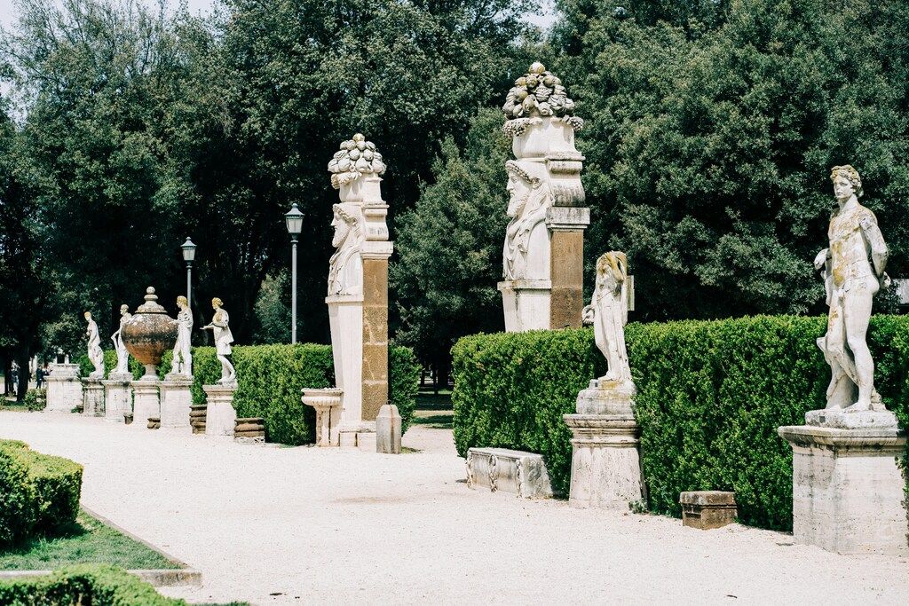 Entrance to one of the gardens of Villa Borghese with classical statues and sculpted hedges in a lush garden setting.