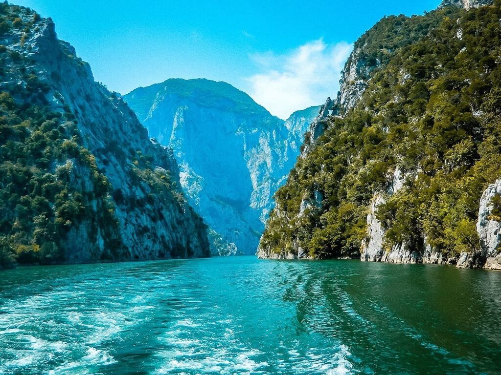 River view surrounded by steep, forested cliffs, with clear turquoise water flowing between the mountainous terrain in Albania