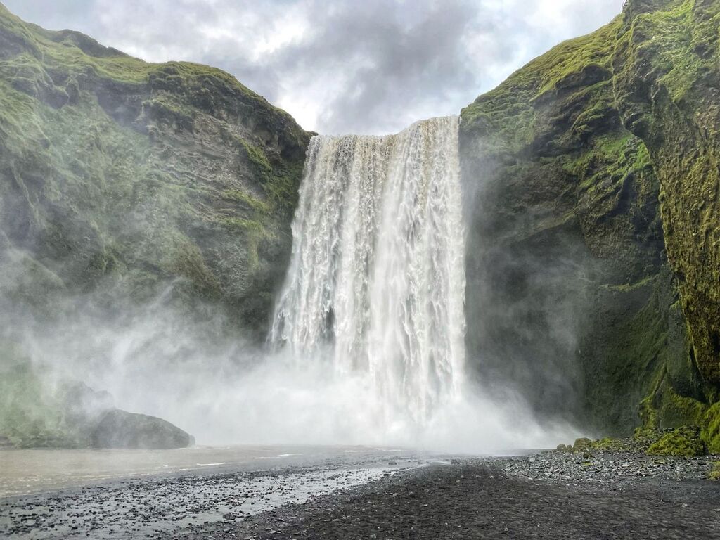 Powerful waterfall cascading down a steep, moss-covered cliff, surrounded by mist and lush greenery in Iceland