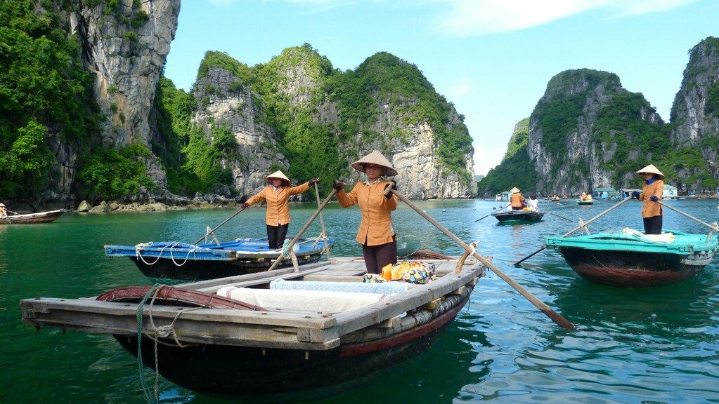 Local women rowing traditional wooden boats through the emerald waters of Halong Bay, Vietnam