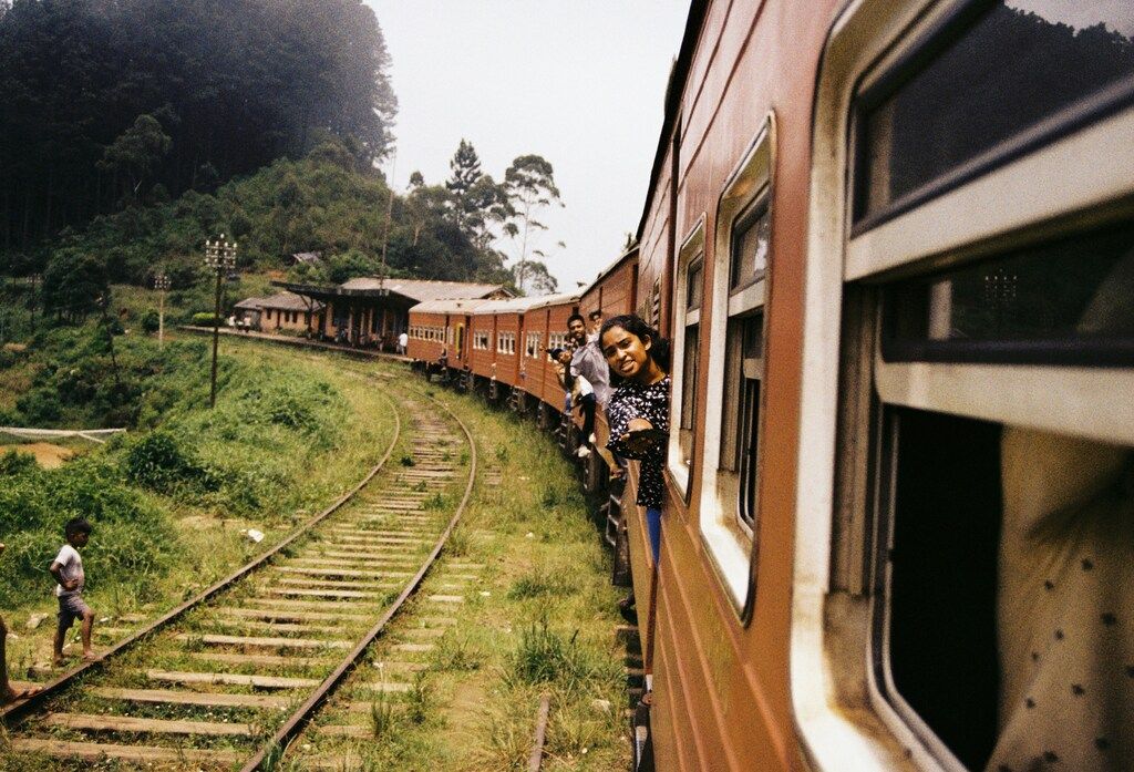 Passengers lean out of the windows of a red train in Sri Lanka