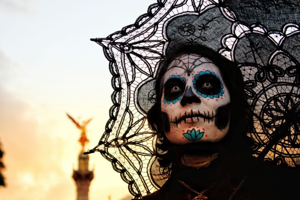 A person with intricate sugar skull face paint and a black lace veil celebrates Día de los Muertos