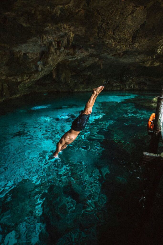 A man dives gracefully into the crystal-clear waters of a cenote, surrounded by the natural beauty of an underground cave