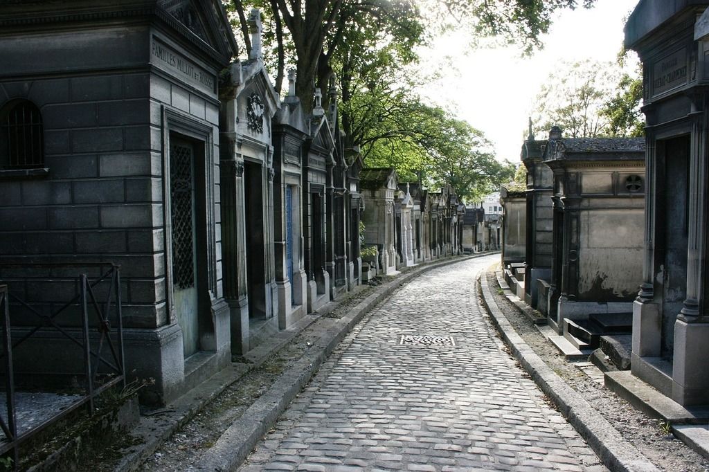 The cobbled pathways of Père Lachaise Cemetery in Paris, surrounded by historic tombs and tall trees.