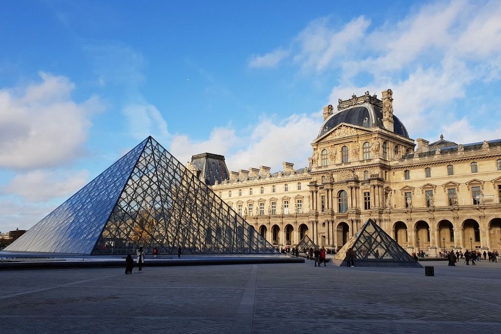 The Louvre Museum and its modern glass pyramid in Paris, framed by a bright blue sky.