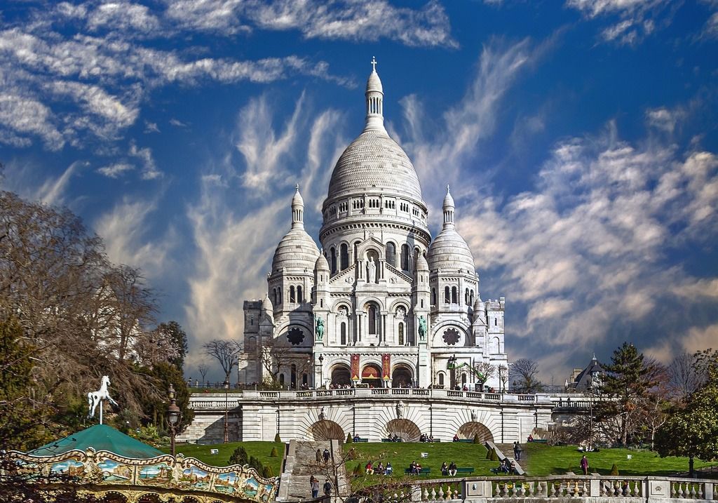 The Sacré-Cœur Basilica in Paris, with its white domes, against a dramatic sky of swirling clouds