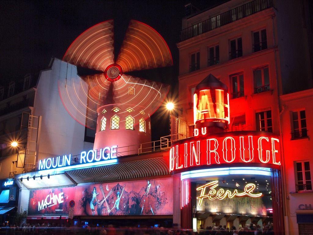 The illuminated Moulin Rouge in Paris at night, with its iconic red windmill spinning brightly.