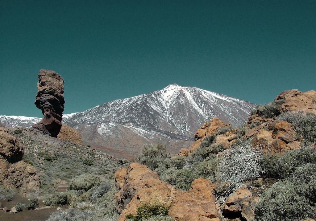 Snow-capped Mount Teide in Tenerife, surrounded by volcanic rock formations and clear blue skies.