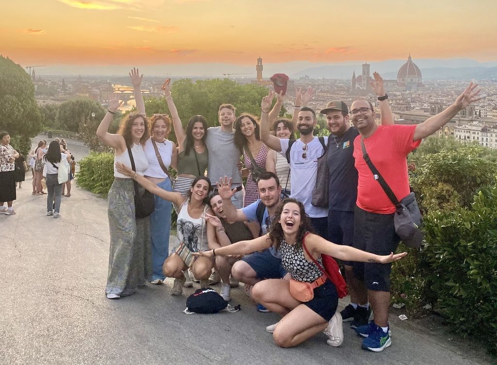 Group photo during a WeRoad organized trip to Florence, Italy, capturing the sunset over the city from Piazzale Michelangelo.