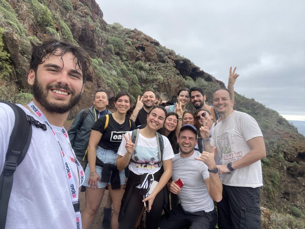 A group of smiling travelers on a hiking adventure in Tenerife with lush mountains in the background, part of a WeRoad group tour.