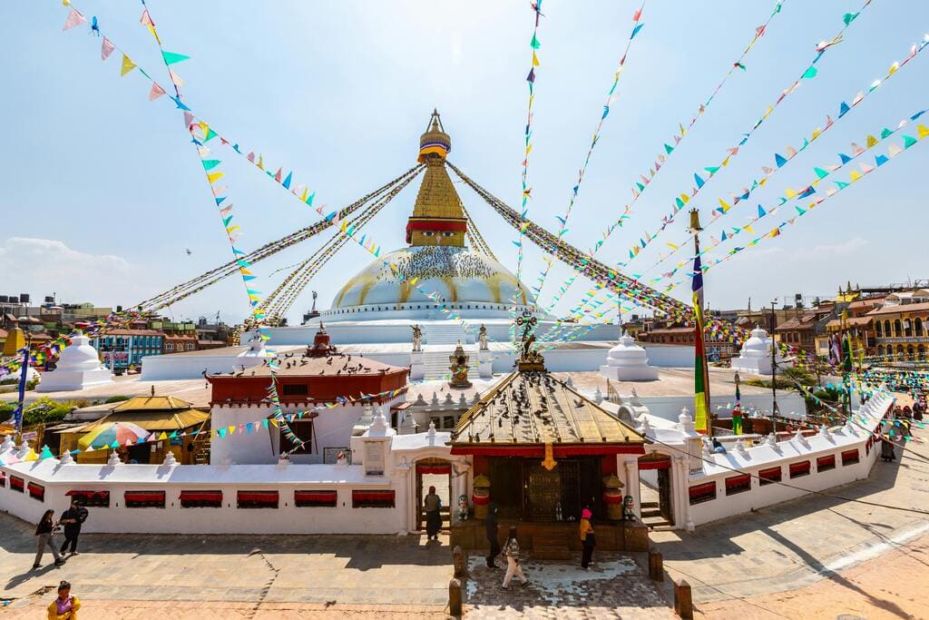 Boudhanath Stupa in Kathmandu, Nepal, adorned with colorful prayer flags on a sunny day.