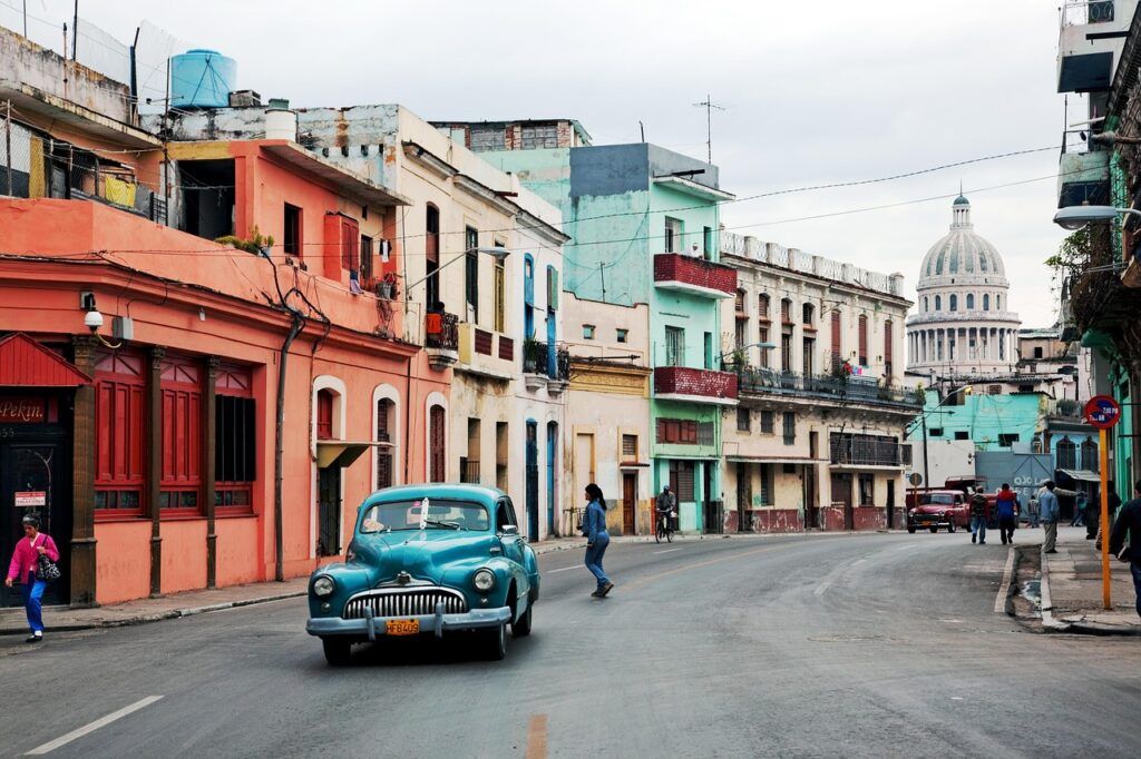 Colorful street in Havana, Cuba, with a vintage car and the Capitolio building in the background.