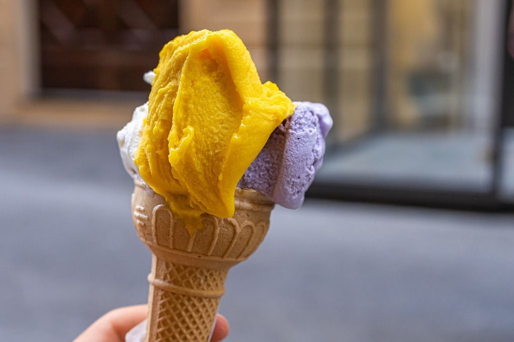 Close-up of a colorful gelato cone, showcasing vibrant flavors of mango and lavender, in Florence, Italy.