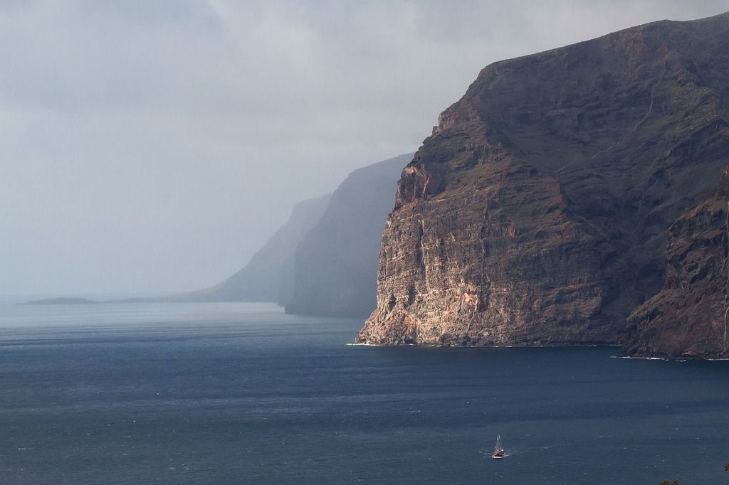 Los Gigantes cliffs in Tenerife, rising dramatically from the ocean, with a small sailboat in the distance.