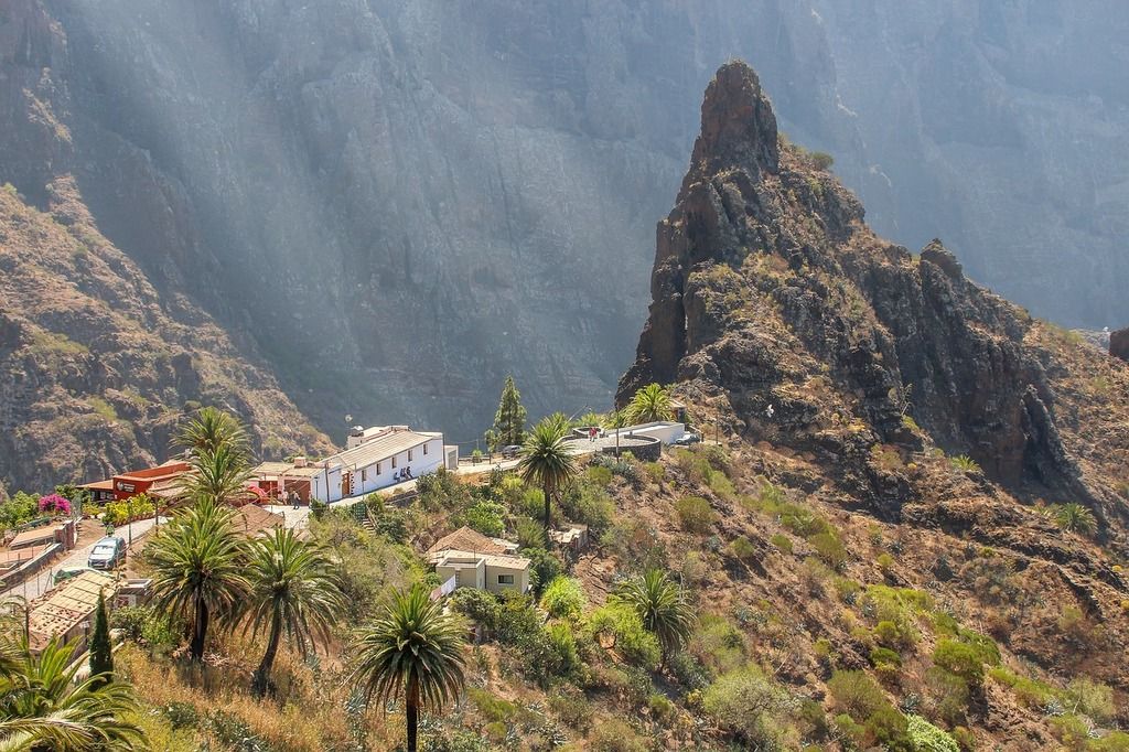 The village of Masca in Tenerife, surrounded by rugged mountain peaks and palm trees under a hazy sky.