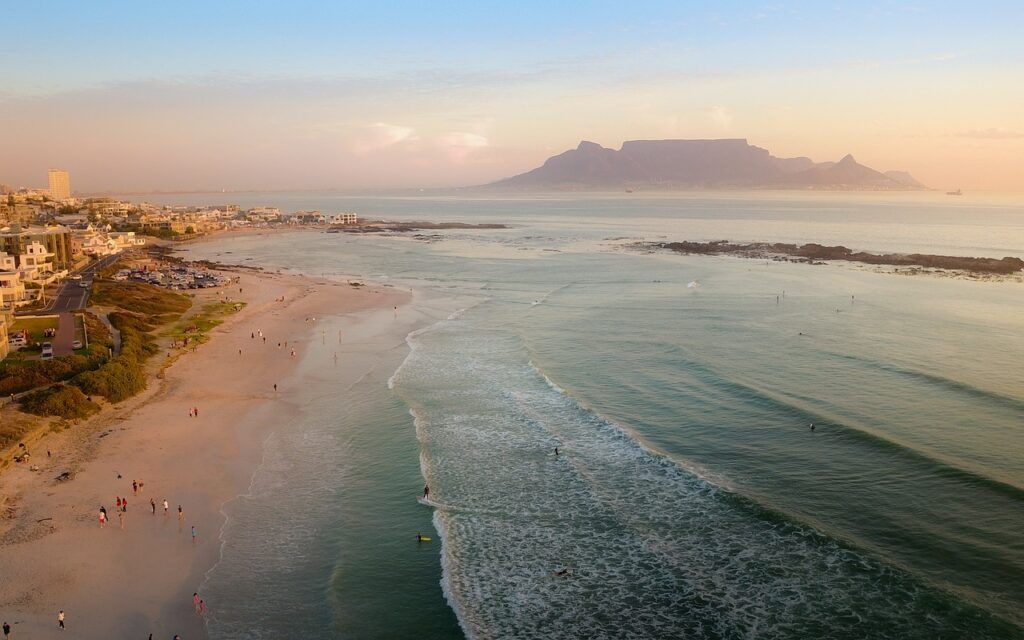 Beach in Cape Town, South Africa, with waves rolling in and Table Mountain visible in the distance.