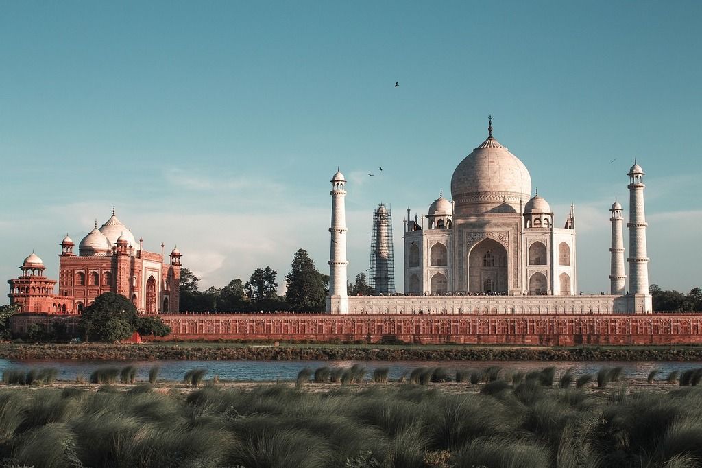 The Taj Mahal in India with a red sandstone building on the left and a clear blue sky.