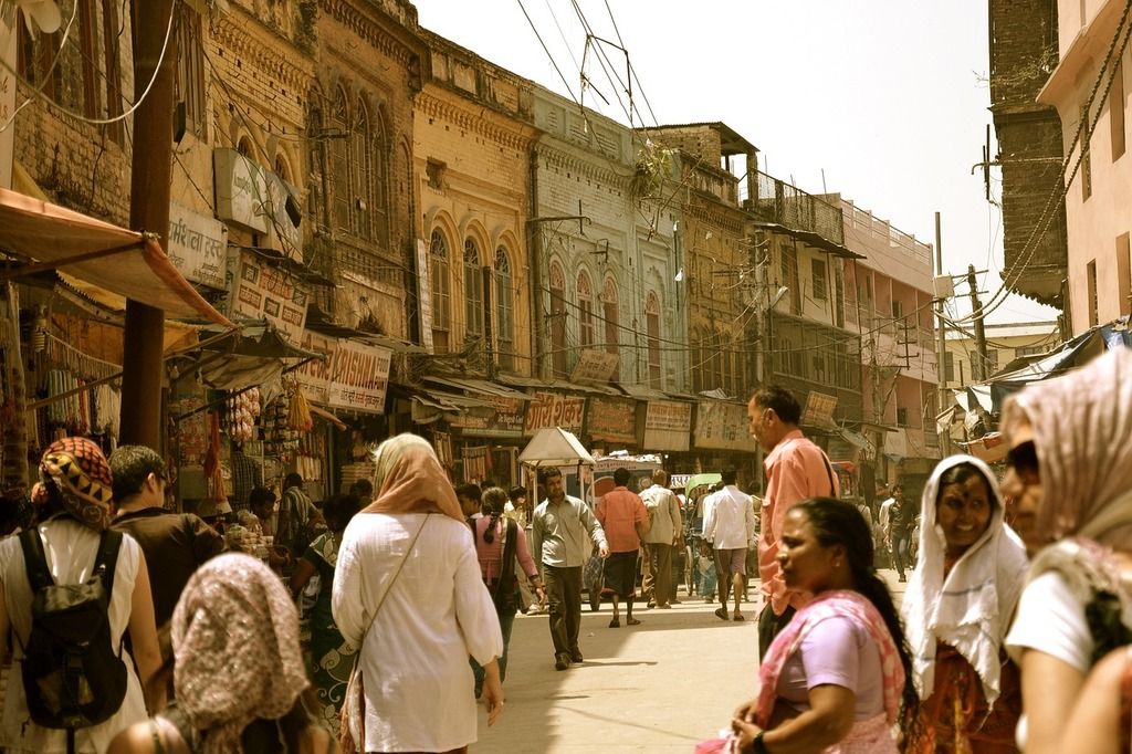 Busy street market in India with people walking and historic buildings in the background.