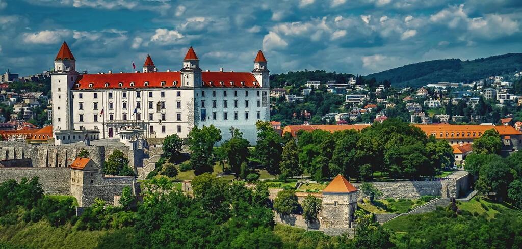 Panoramic view of Bratislava Castle with its red roof and white walls surrounded by lush greenery.