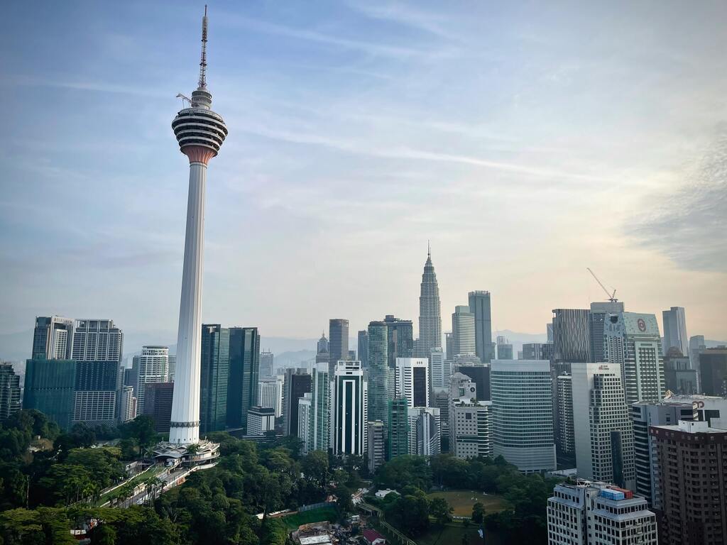 Skyline of Kuala Lumpur featuring the iconic KL Tower and Petronas Twin Towers surrounded by modern skyscrapers and lush greenery.