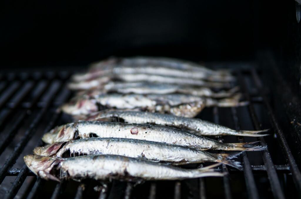 Grilled sardines cooking on a barbecue, a classic Portuguese delicacy.