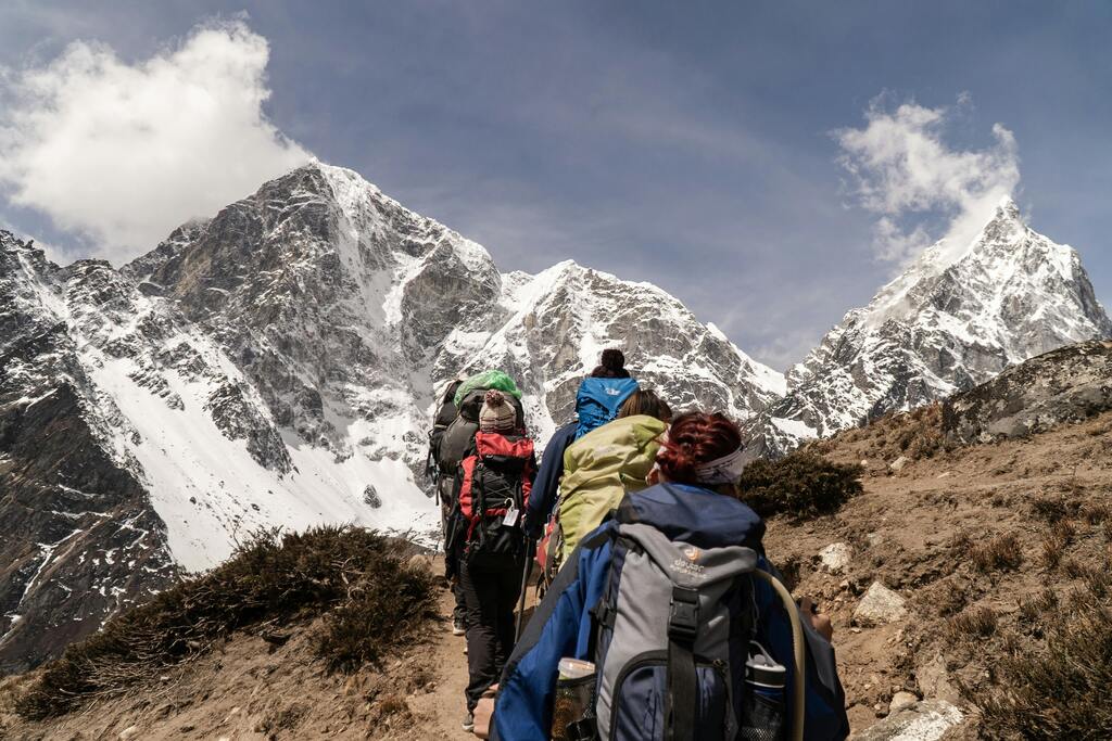 A group of hikers trekking through a mountainous path in Nepal, surrounded by snow-capped peaks.