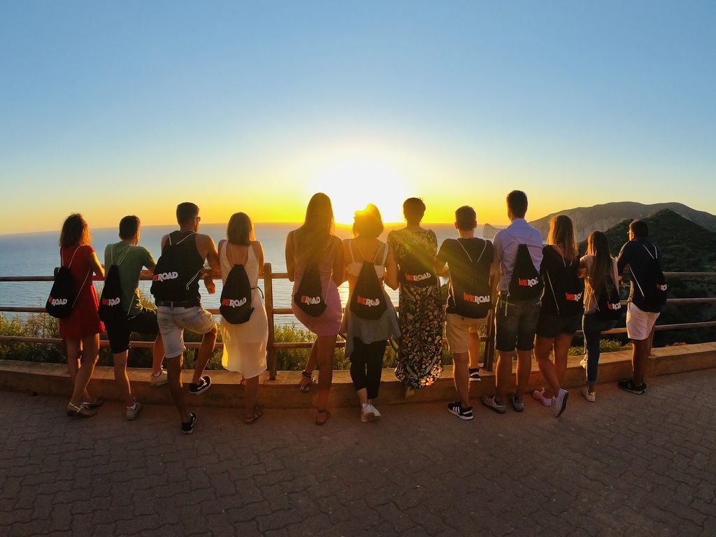 WeRoad group trip in Sardinia, sunset view over the sea with tour backpacks.