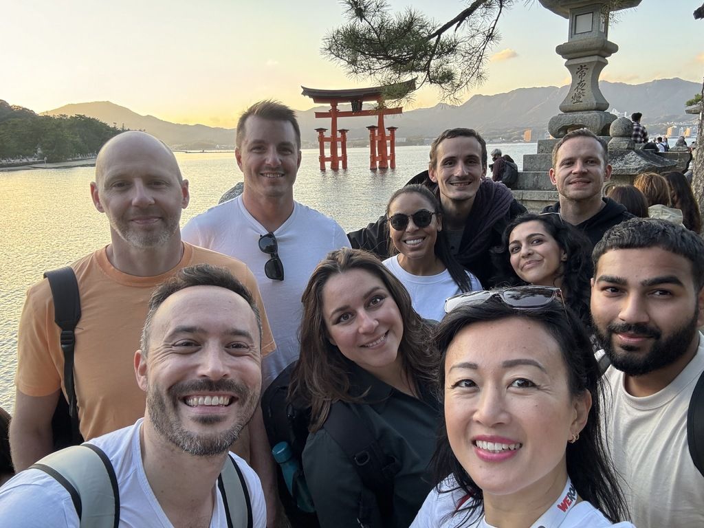 A group of travelers posing in front of the Itsukushima Shrine's floating torii gate in Miyajima, Japan, during a WeRoad organized trip.