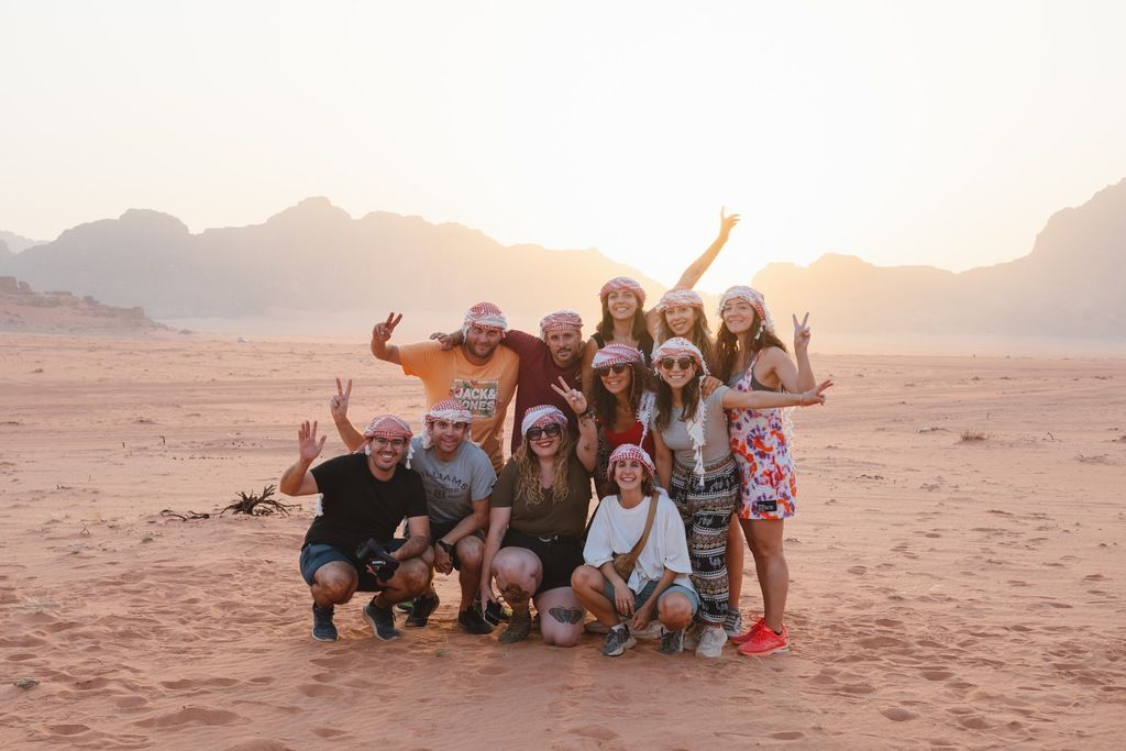 A WeRoad group trip in Jordan posing in Wadi Rum at sunset, wearing traditional keffiyeh scarves.