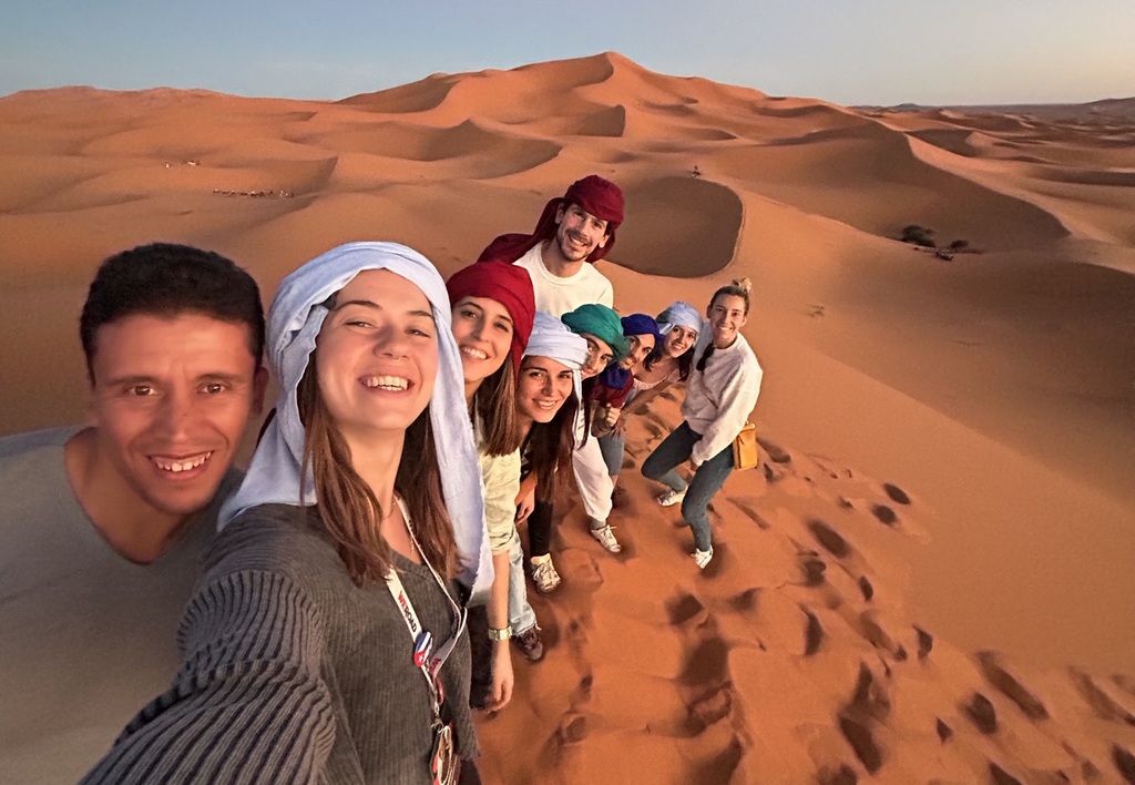 A group of travelers enjoying a sunset in the Moroccan desert as part of a group trip organized by WeRoad.