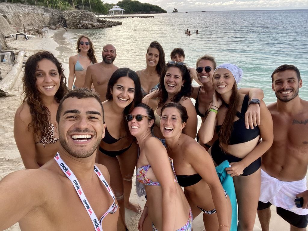 WeRoad group trip on a beach, friends smiling in swimsuits.