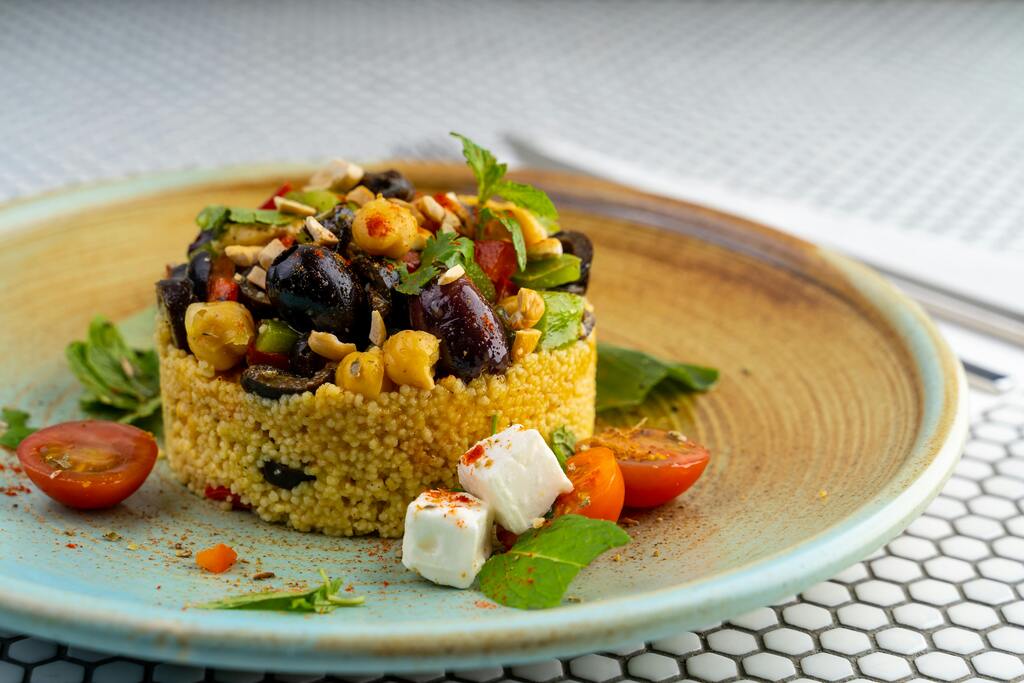 A plate of Moroccan couscous topped with chickpeas, olives, fresh vegetables, and feta cheese, garnished with mint leaves.