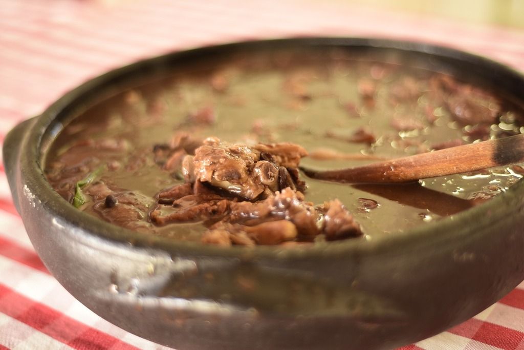 Close-up of a bowl of "feijoada," a traditional Brazilian stew made with beans, pork, and beef, served in a rustic pot.