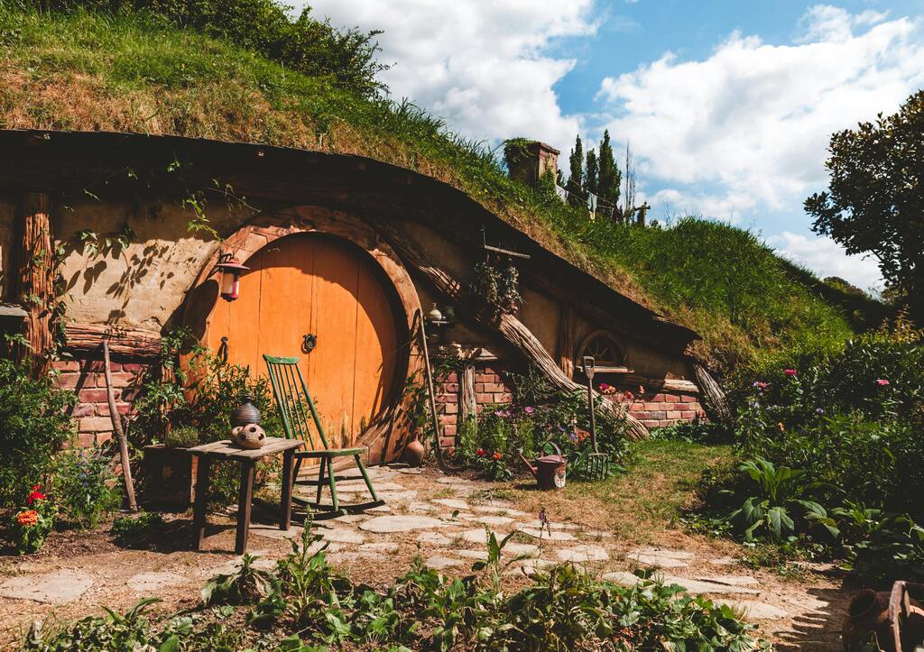 Charming Hobbiton house with a round orange door, nestled in a lush green hill.