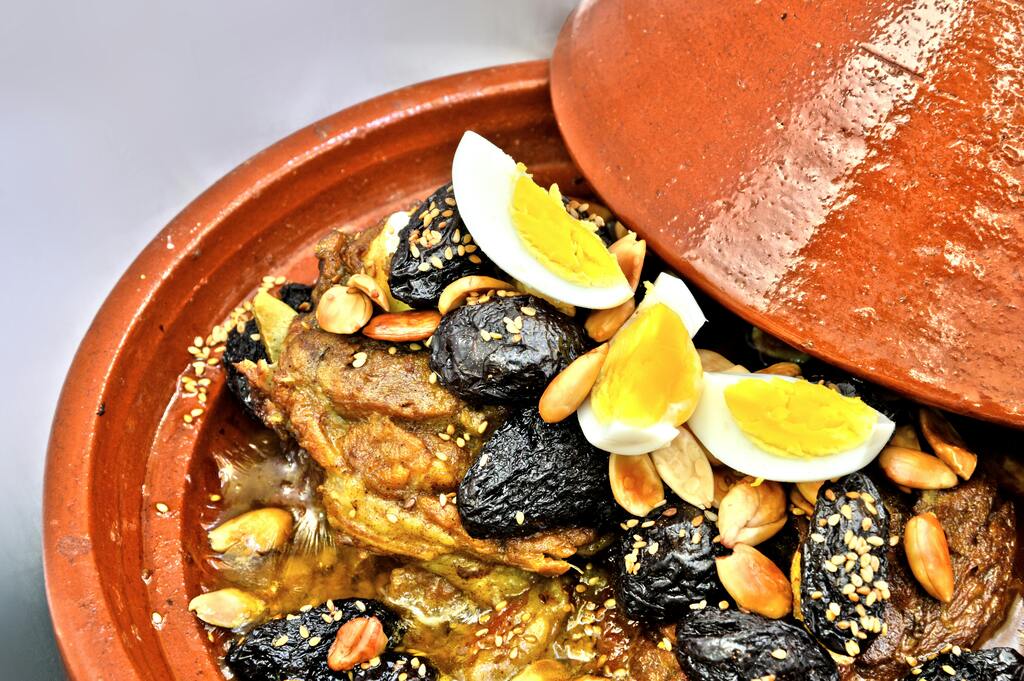 A close-up view of a Moroccan tagine filled with meat, prunes, almonds, and hard-boiled eggs, served in a clay pot.