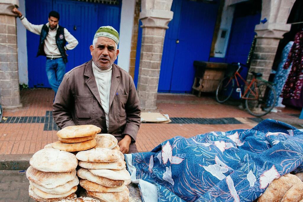 A street vendor selling traditional Moroccan bread at a local market, with stacks of bread displayed.