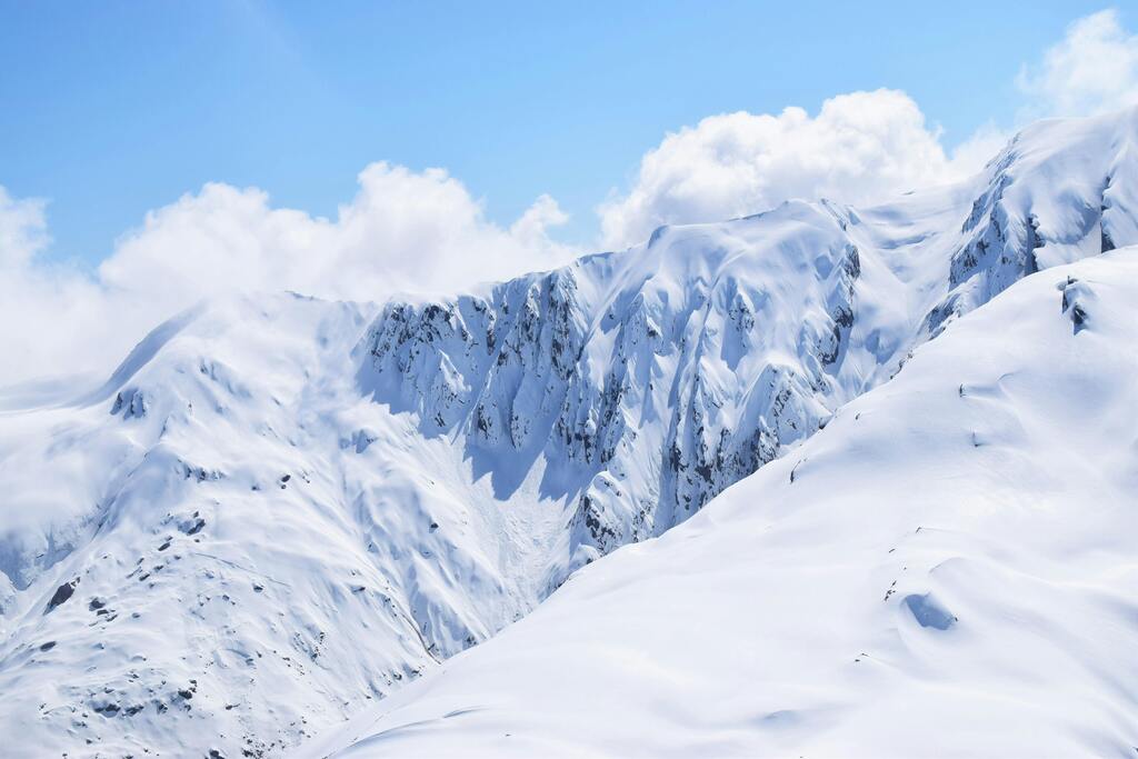 Majestic snow-covered peaks under a bright blue sky with fluffy clouds.